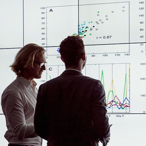 Two students stand in front of giant monitor of data graphs