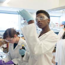 Student in safety goggles looks at a test tube