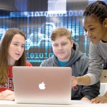 Three students work at a laptop